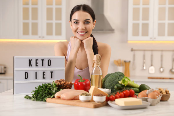 Happy Frau in der Nähe Leuchtkasten mit den Worten Keto Diet und verschiedene Produkte in der Küche