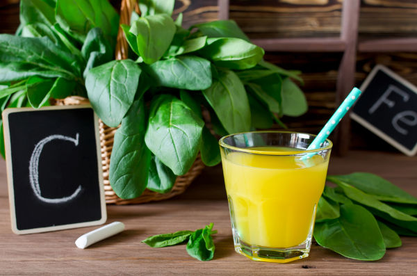 Frischer Spinat in einem Korb und Orangensaft auf dem Tisch. Vitamin C und Eisen enthaltende Produkte. Spinat ist ein jährliches Gemüse, eine Kräuterpflanze der Familie Chenopodiaceae.