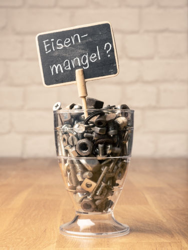 Deutsche Wörter Eisenmangel auf kleiner Tafel in einem Glas mit Schrauben und Nüssen, Gesundheitskonzept