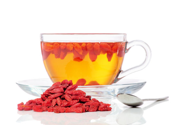 Goji-Beeren Tee in einer glastransparenten Tasse, eine Hefe getrockneter Beeren und Löffel, Nahaufnahme auf weißem Hintergrund einzeln