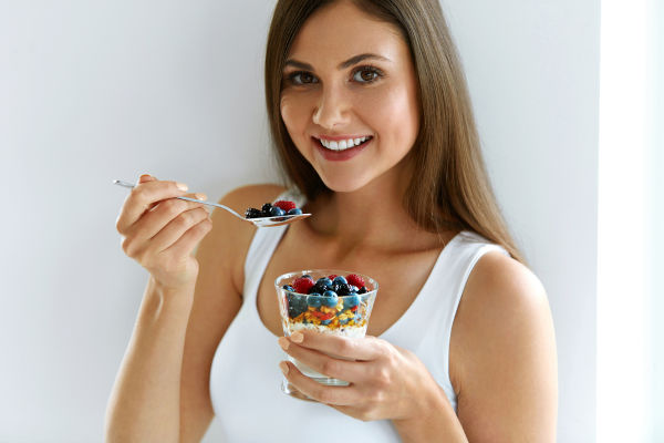 Gesundes Gewicht verliert Nahrung. Portrait von ziemlich lächelnden Fit Girl mit Jogurt, Berries und Haferflocken. Schöne junge Frau, die zum Frühstück frisch Jogurt, Berries und Granola isst. Ernährungskonzept