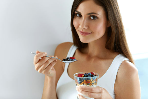 Weibliche auf gesunde Ernährung. Nahaufnahme von lächelnden jungen Frauen mit Glas Bio-Jogurt, frischen Bereren und Rohmuesli. Schönes glückliches Mädchen essen Diät Jogurt Oats Dessert zum Frühstück.