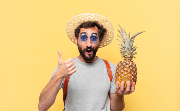junge verrückte Reisende Mann glücklich Ausdruck und hält eine Ananas
