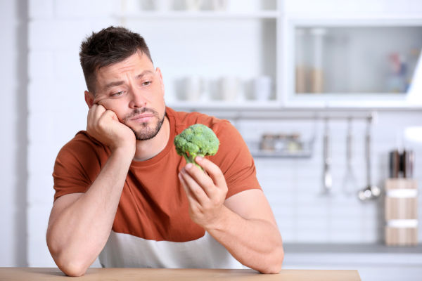 Porträt eines unglücklichen Mannes mit Brokkoli am Tisch in der Küche