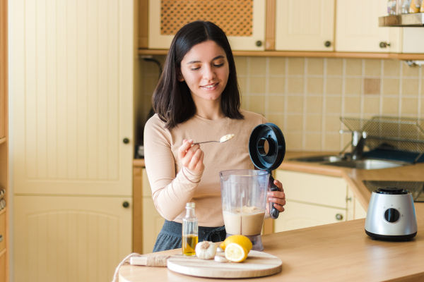 attraktive Frau mit schönem Lächeln in der Küche bereiten natürliche vegetarische Speisen. hausgemachte Kichererbsen-Hummus-Rezeptur