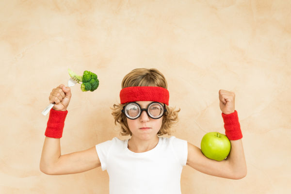 Sportrsman Nerd Kind isst Superfood. Geek Kind hält Brokkoli und Apfel. Gesunde Ernährung und Lebensstil Konzept. Grünes vegetarisches Essen
