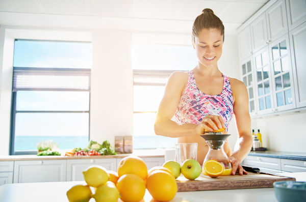 Fit lächelnde junge Frau, die gesunde Fruchtsäfte aus einem Sortiment frischer Früchte zubereitet, mit einem manuellen Saft in ihrer Küche , Kopienraum auf einem hohen Schlüsselhintergrund