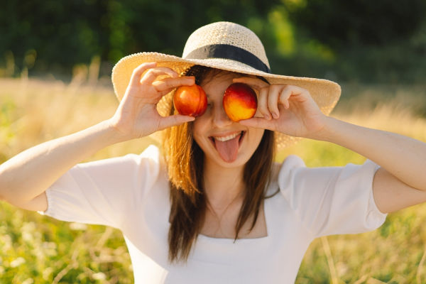 Schönes, sorgenfreies Sommermädchen im Freien mit orangefarbenen Pfirsichfrüchten. Junge Frau isst Pfirsich. Sommerpicknickstimmung.